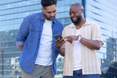 Cuadro en lienzo Two male friends standing in urban plaza outside modern glass office building, s