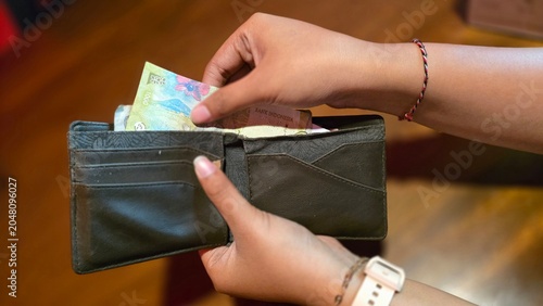 Obraz na plátně Indonesian woman holding open wallet with Indonesian rupiah banknotes, close-up view on wooden table background