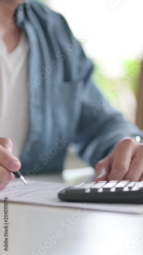 Hands of Man Writing on Paper, using Calculator, Vertical Video