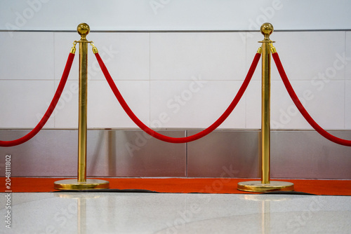 Schilderij op canvas Gold metal stanchions with velvet rope stand on red carpet near wall tile at entrance area of standard cinema building