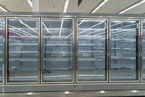 Row of completely empty commercial supermarket glass door refrigerator cabinets standing inside an unstocked retail grocery store.