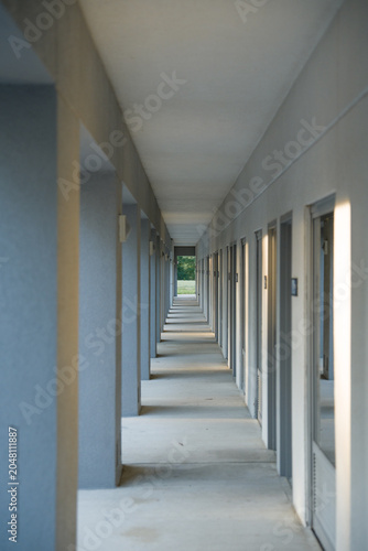 Photography Long empty outdoor concrete corridor with grey architectural pillars and repeating doors diminishing into a deep perspective