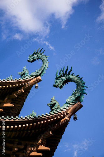 Obraz na płótnie Twin dragon sculptures rise from a traditional temple roof against a bright blue sky
