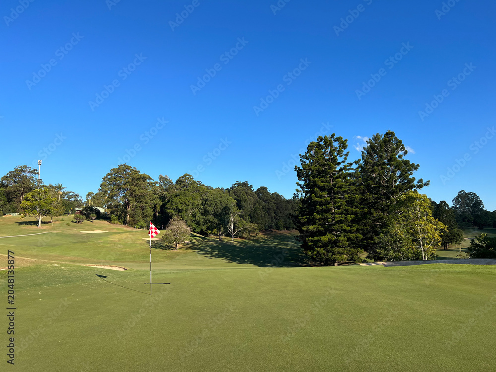 Obraz premium Scenic Golf Course Green with Red Checkered Flag Under Blue Sky