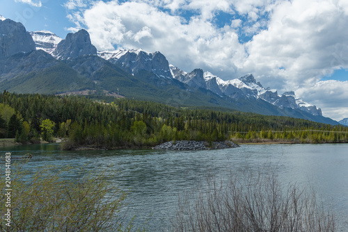 Stunning summertime views in Canada along the Bow River in the town of Canmore with stunning, snow capped peaks in small tourist town. 
