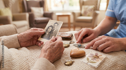 Elderly hands holding vintage black and white photograph of young couple, wrinkled skin and nostalgic personal keepsakes on blanket, showing mementos to healthcare worker, senior care