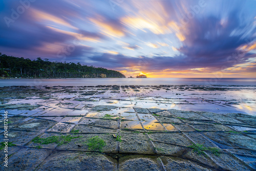 Fotografie Sunrise over the famous Tessellated Pavement on the Tasman Peninsula, Tasmania, featuring dramatic clouds, reflections and unique geometric coastal rock formations
