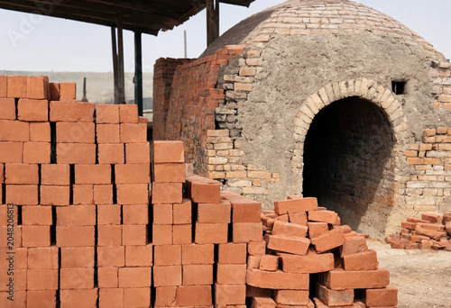 Photos Large stack of red clay bricks next to a traditional round brick kiln structure