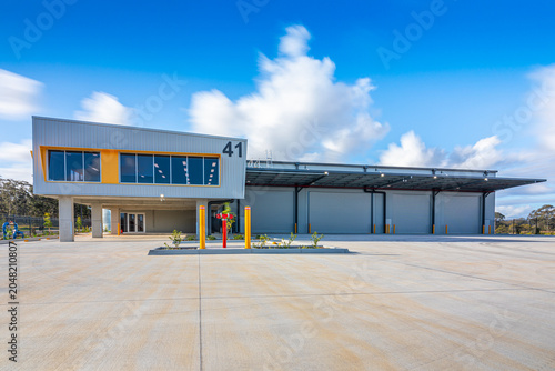 Canvastavla Modern industrial warehouse and office facility with multiple roller doors, loading area and expansive concrete hardstand under a blue sky