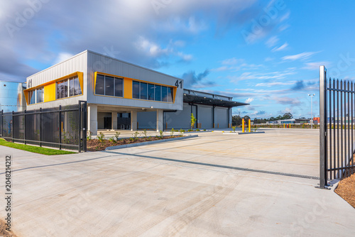Foto Secure industrial warehouse facility viewed through gated entrance with office accommodation, loading bays and large vehicle manoeuvring area