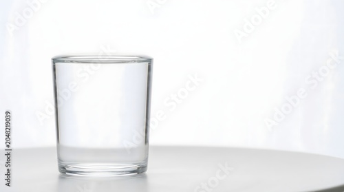 Plain clear glass filled exactly to brim with water showing surface tension meniscus in morning light on white surface, contentment enough gratitude states of mind concept art 
