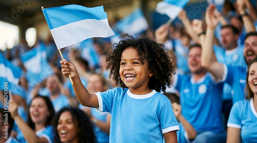 A happy young child waving a blue and white flag at a crowded sports stadium