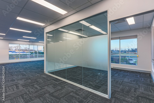 Cuadro en lienzo Modern office interior with glass partition meeting room, open-plan workspace, carpet tile flooring and large windows overlooking a commercial estate