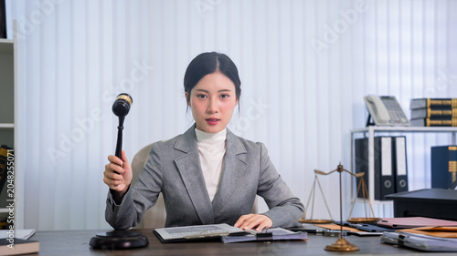 Asian women lawyer judge holding gavel sitting desk law office courtroom professional attorney legal justice workspace barrister solicitor counselor advocate