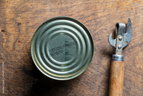 Fotografie Closed tin can with expiration date and vintage opener on wooden table