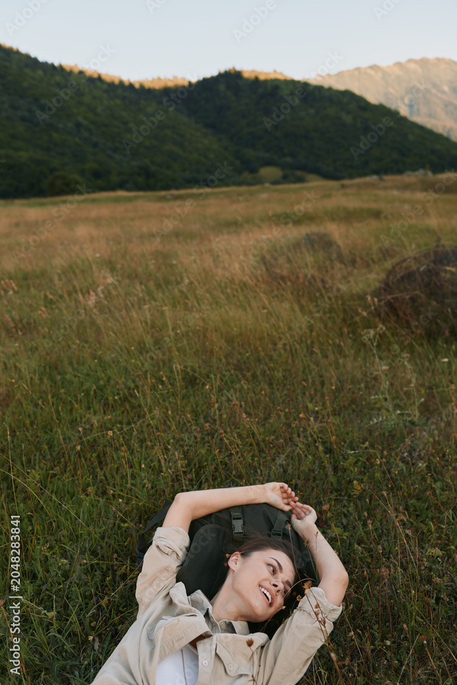 Naklejka premium Young woman with short brown hair lies on tall grass in a natural field surrounded by hills, enjoying a peaceful moment with a relaxed and content expression.
