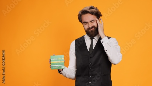 Tableau sur toile Classy waiter with headache recommends pills on camera, showcasing pack of painkillers to ease pain