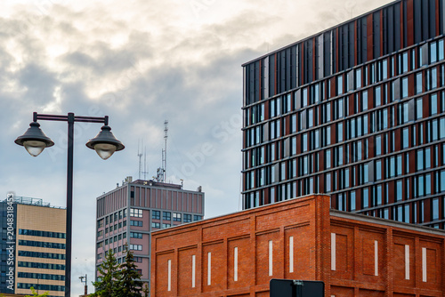 Foto Cityscape of Lodz showcasing contrasting architecture with an old red brick industrial building in the foreground, modern glass skyscraper, high-rise blocks, street lantern and cloudy sky
