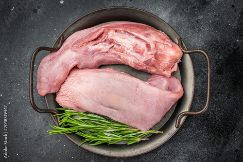 Whole raw uncooked pork tongue offal in skillet with herbs and vintage fork top view on dark background perfect for cuisine and butchery themes