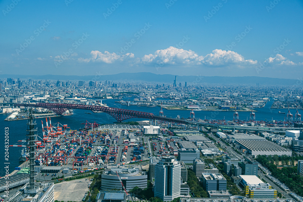Naklejka premium Aerial View of Osaka Port Container Terminal with Red Arch Bridge and City Skyline