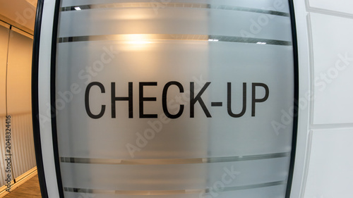 Close-up of a check-up text sign on a frosted glass door in a modern, clean medical clinic or hospital interior. Healthcare, wellness, and medical examination concept.