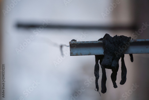 Schilderij op canvas A single dark fabric work glove hangs over a rusted metal beam, appearing worn and used, in an ambiguous indoor or sheltered outdoor setting