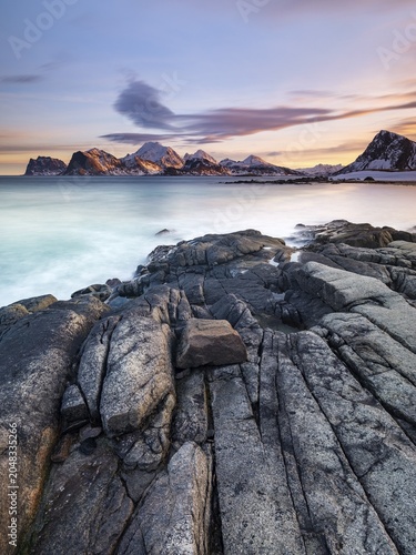 Rocky coast, snow-capped mountains in the background, Vestvågøya, Lofoten, Norway