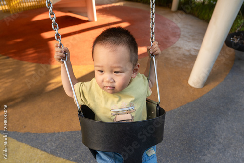 Toddler boy sitting in playground swing