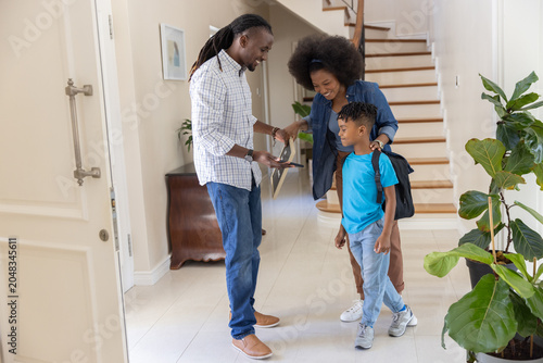 African American family preparing at entry hall, father holding keys while child wearing backpack