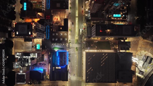 Top down cityscape of downtown Los Angeles at night, showcasing illuminated skyscrapers, bustling streets with vehicle traffic, rooftop pools, modern urban architecture