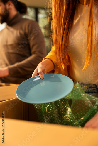 Close up of woman unpacking home items wrapped in cardboard boxes, ensuring settlement in their new house, People arranging furniture and decorations after moving day, life event.