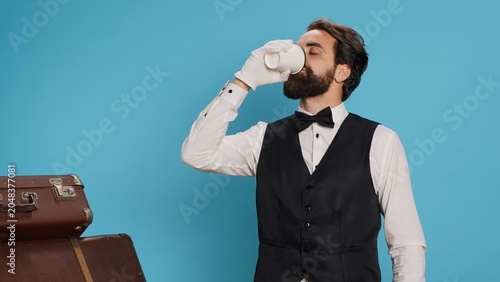 Foto Hotel porter drinking coffee on camera, bellboy wearing luxurious clothes and white gloves