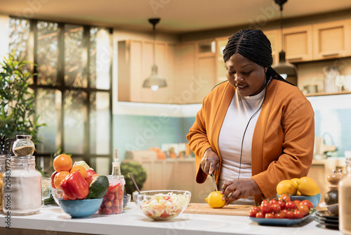 Fényképezés African American woman cutting lemon for salad seasoning with sour juice, recording a food vlog episode in a modern home kitchen, Content creator focuses on healthy ingredients and vegetables