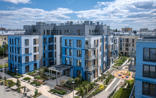 Aerial view showcases a contemporary multi-story residential building with varying shades of blue and neutral tones. It features balconies