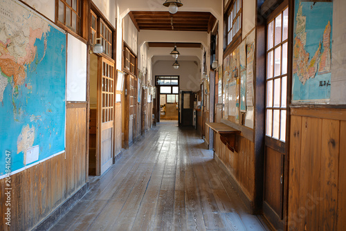 Long corridor featuring wood paneling, maps, & framed displays. Overhead lighting brightens the view to the distant end, where a doorway awaits