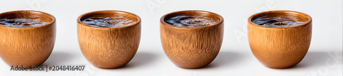 Four identical, wooden cups, each filled with a dark liquid, are arranged in a row against a plain white background