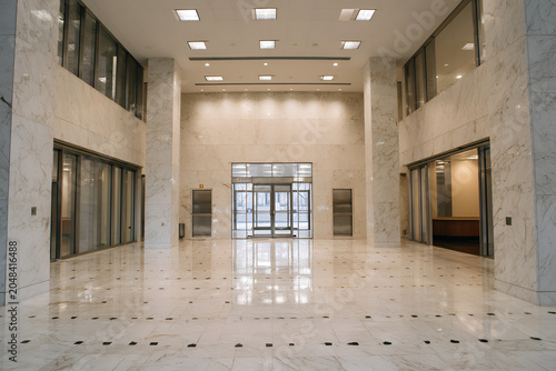 Expansive lobby of a modern building, showcasing marble flooring and walls, multiple entryways, and ample natural light