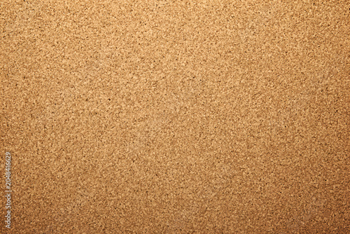 Close-up view of a standard corkboard texture. It has a warm brown color and many small specks, used for bulletin boards