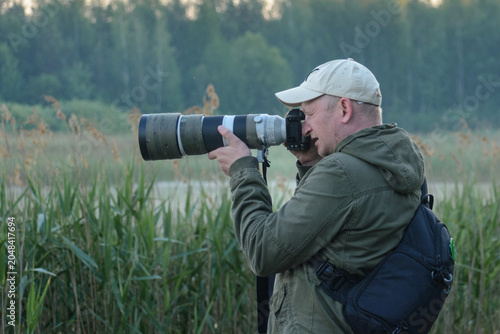 Bild auf Leinwand A photographer in a green jacket and cap uses a large telephoto lens to capture