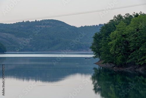 Obraz na plátne Serene horizontal landscape of Lake Plastira in Greece, featuring a dense green forest reflecting beautifully in the calm, mirror-like water at twilight