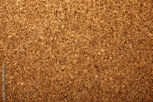 A close-up shot of a corkboard surface with a textured, granulated pattern. The brown color palette gives a natural feel