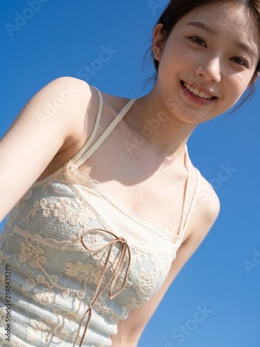A Joyful Gaze Under the Summer Sky: A young woman with a radiant smile, her eyes sparkling with happiness, looks down from a low-angle perspective against a clear blue sky.