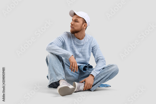 Stylish young man in cap sitting on light background