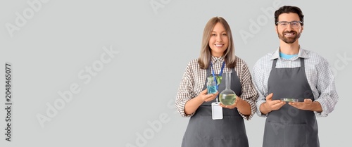Agricultural engineers with plant samples and flask on light background with ...