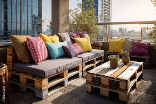 Rooftop patio furniture made from wooden pallets and colorful cushions. Use it to illustrate outdoor living, sustainable design, or urban relaxation.