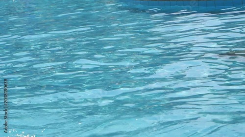 High-angle close-up of crystal clear blue water rippling gently in a swimming pool, reflecting bright daylight.