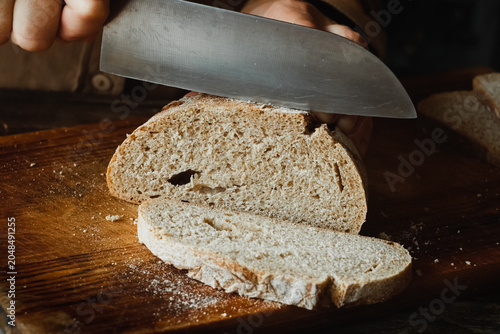Slicing freshly baked brown bread on cutting board