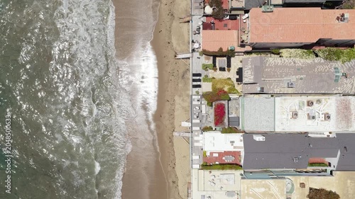 Top down overhead real estate shot flying above expensive waterfront property and beach homes lining ocean shore in exclusive Malibu, California neighborhood