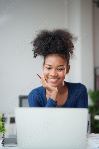 Young smiling African American woman with pencil in hand watching content on laptop, studying online, learning new skills, working remotely or consulting an entrepreneurship project from home
