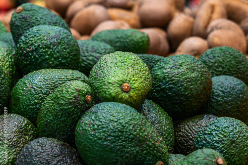 Fresh ripe hass avocado pile close up at grocery store or market. Raw vegan food ingredients for healthy diet lifestyle and culinary blog background